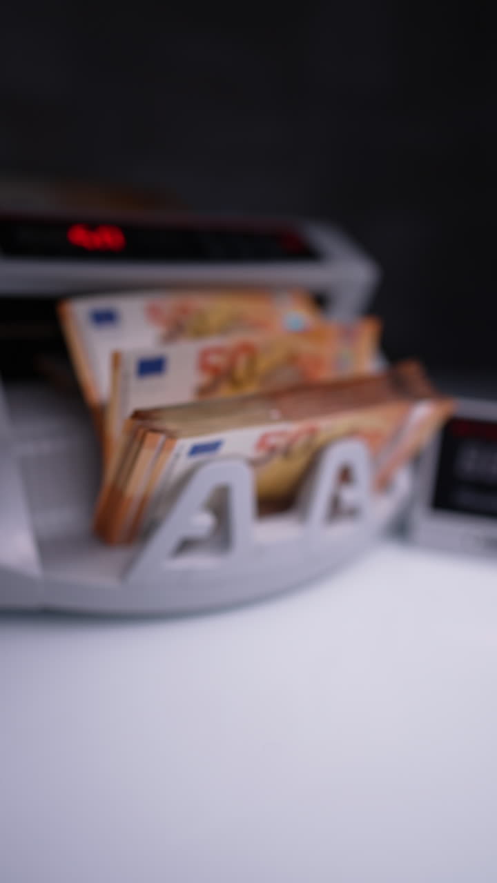 Orange fifty euro bills processed in cash counting machine. Hand takes money and puts a stack in front of device. Close up. Blurred image. Vertical video.
