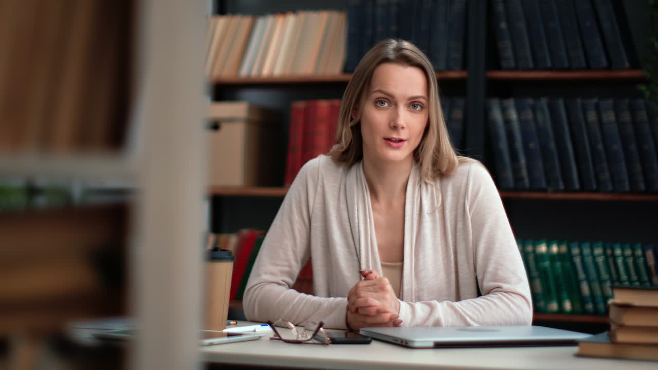 Portret kobiety blogerki rozmawiającej na audytorium, biznes, edukacja, komunikacja, pozującej przy biurku w bibliotece