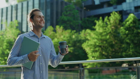 smiling man walking outdoors with laptop and coffee