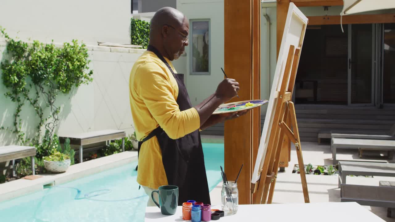 African american senior man standing on a terrace and painting