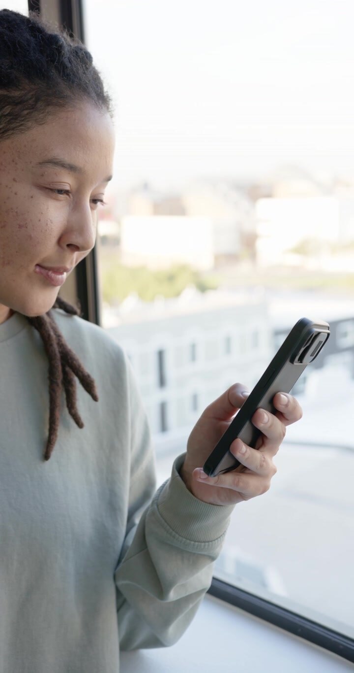 Vertical video: African American non-binary glancing, checking phone text at window, copy space