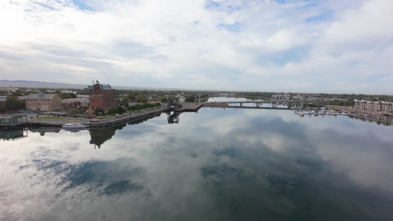 drone flight over port river in port adelaide, the water is calm and reflecting the clouds, there is a bridge and an old historic harts mill on the bank