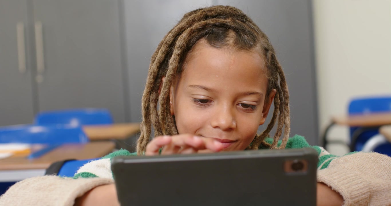 Scolaro afroamericano che tocca un tablet in una custodia scura al banco in classe, seguendo un'app di apprendimento.