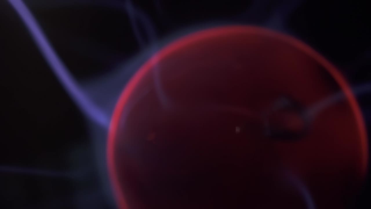 Primo piano macro al rallentatore di una lampada al plasma con scariche elettriche che vanno in tutte le direzioni, con una sfera rossa al centro e uno sfondo nero.