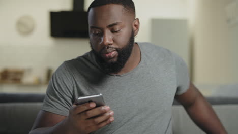 black man holding phone at open kitchen. concentrated guy texting in smartphone.