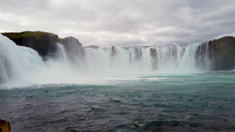 Majestic-Godafoss-waterfall-in-Iceland,-low-pan-at-base-of-river-Skjálfandafljót-with-tourists-on-cliff,-12-meters-39-feet-high,-4k-ProRezHQ