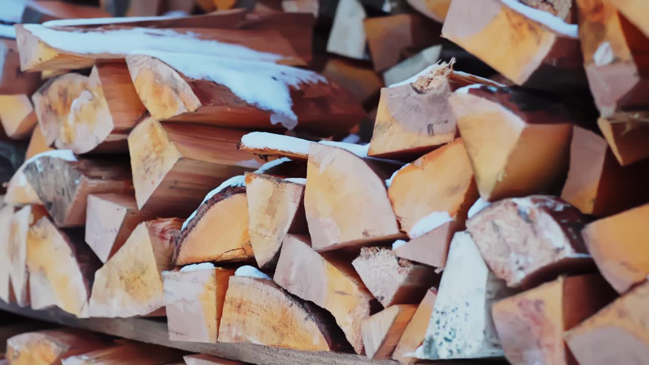Side-view close-up of split firewood stacked with snow, rustic outdoor storage for home heating, cozy winter fuel supply background
