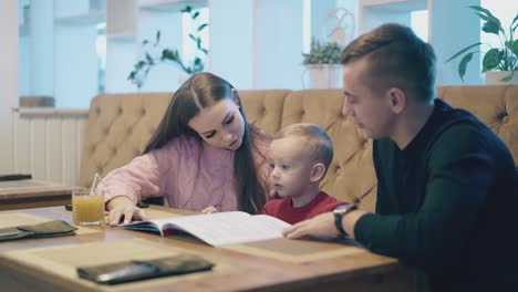 man-in-black-shirt-sits-with-wife-and-child-in-restaurant