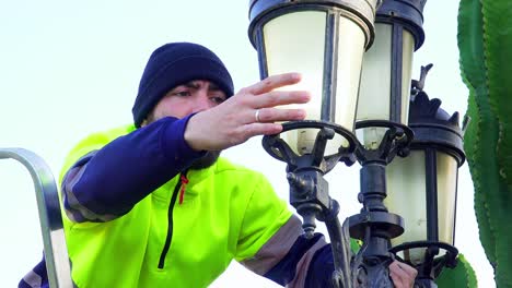 primer plano de un electricista en ropa de trabajo comprobando el montaje de una farola con un cactus cerca