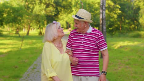 senior old stylish tourists couple grandmother, grandfather having a walk and talking in summer park