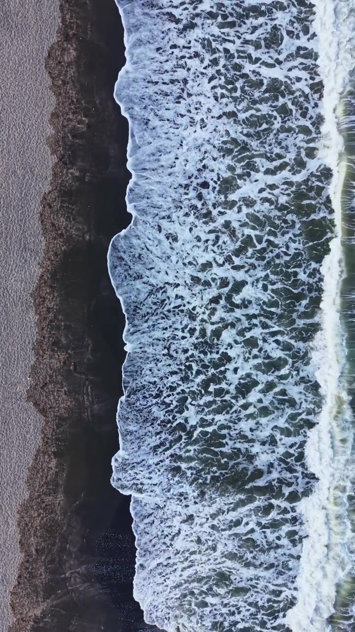 Le onde si infrangono sulla riva di una spiaggia durante le ore diurne in una zona costiera con sabbia e ciottoli.
