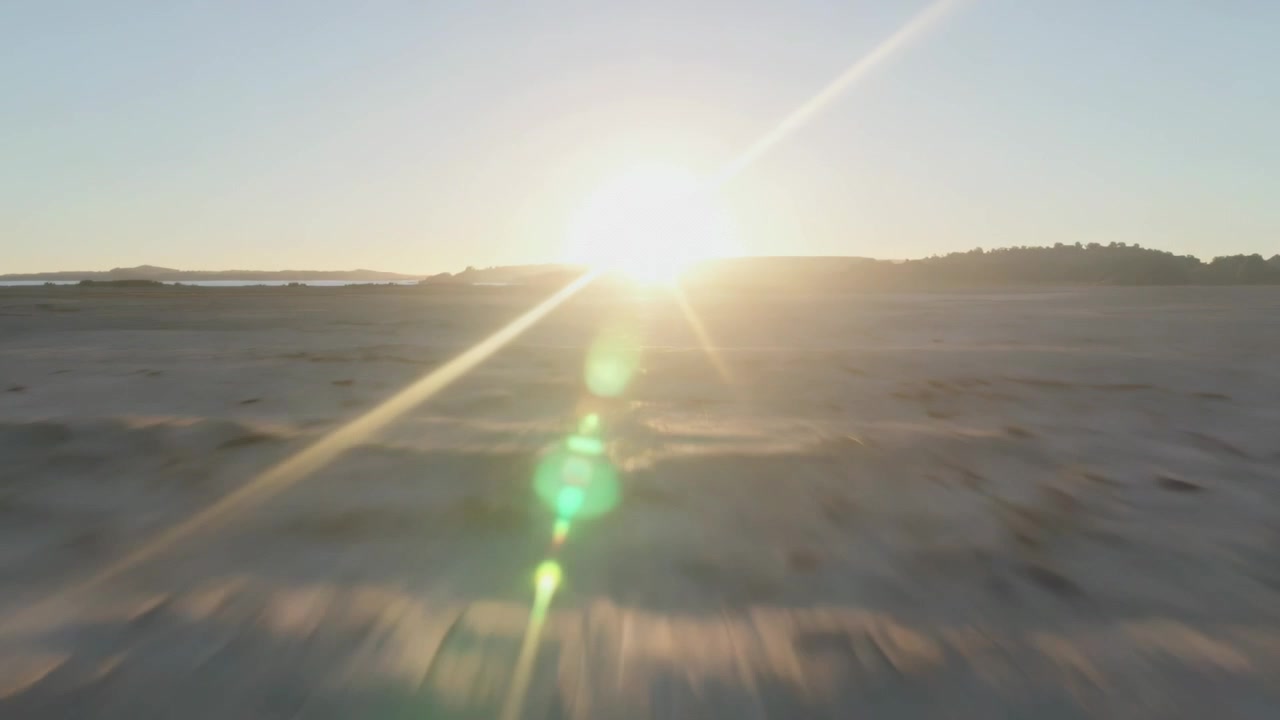 Sol nascente iluminando planície plana e névoa, projetando raios em forma de estrela e reflexo de lente verde para baixo