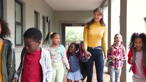 teacher walking with diverse group of happy children at school hallway