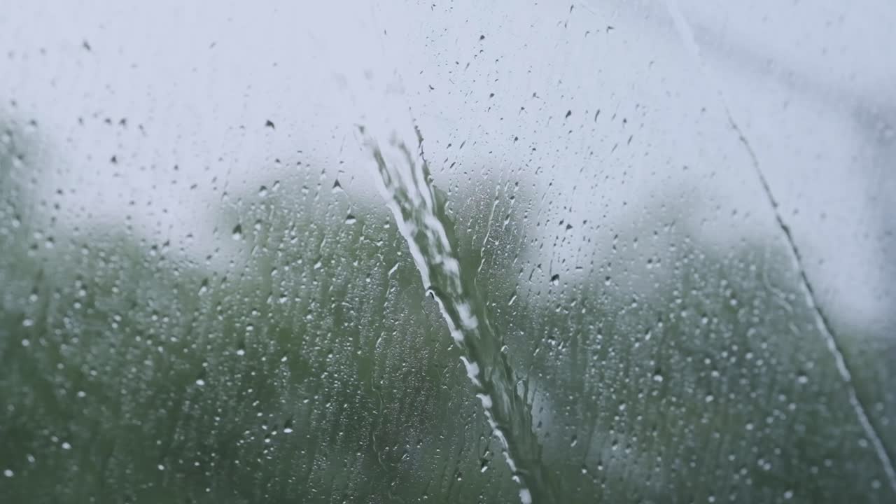 Raindrops slide down train windows revealing a dramatic moving landscape passing outside