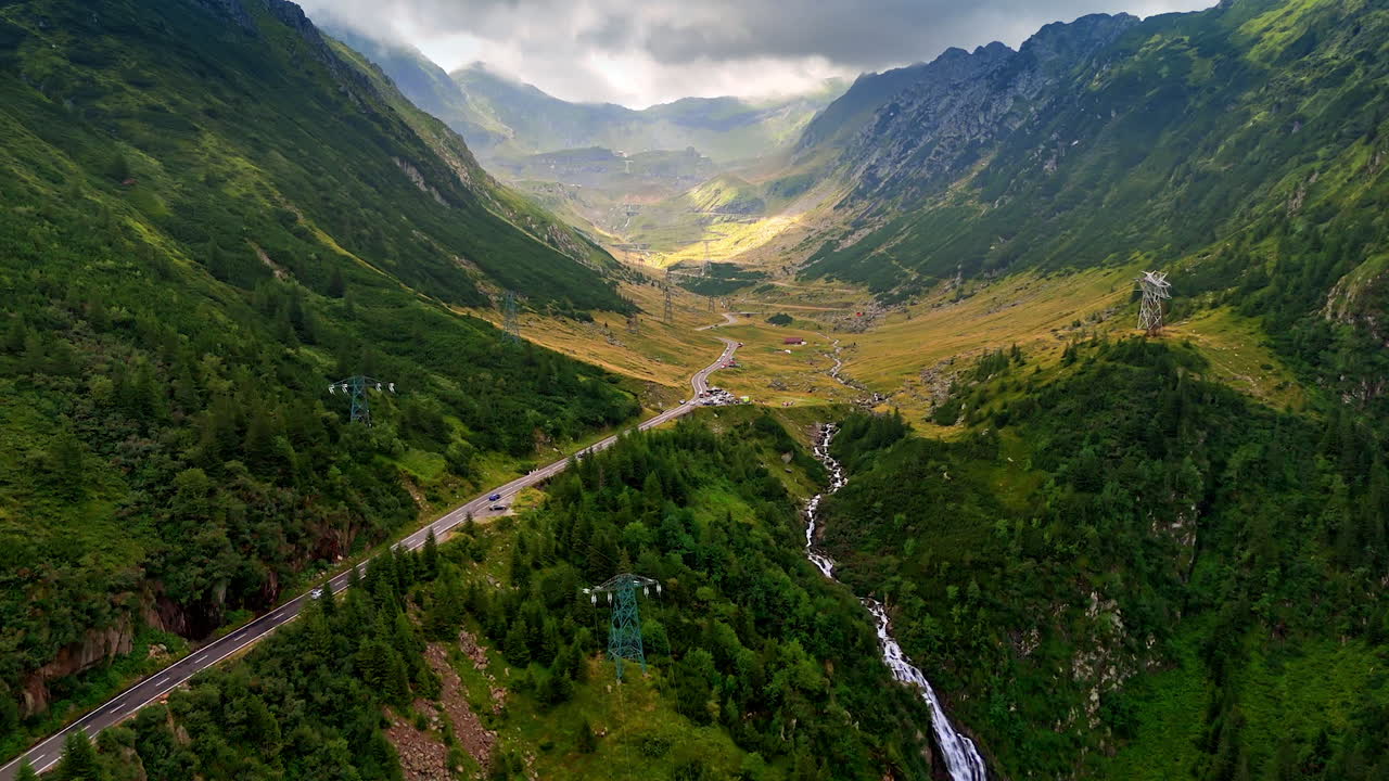 Il trasporto si muove sull'autostrada lungo le montagne verdeggianti. Stretto fiume che scorre attraverso la valle cade dal pendio. Nuvole suggestive coprono il cielo tra le rocce sullo sfondo. Vista aerea. Romania, Monti Carpazi