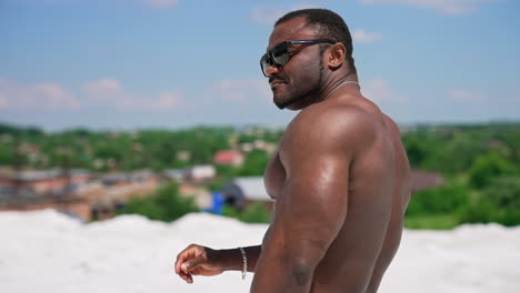 dark skinned bodybuilder in black glasses. back muscles of african american sportsman. shirtless black athlete posing outdoors in summer.