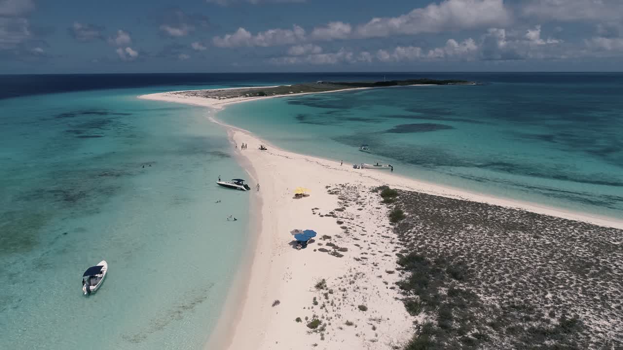 giro aéreo alrededor de la gente en la playa de arena blanca, botes, sombrillas y mar caribe turquesa