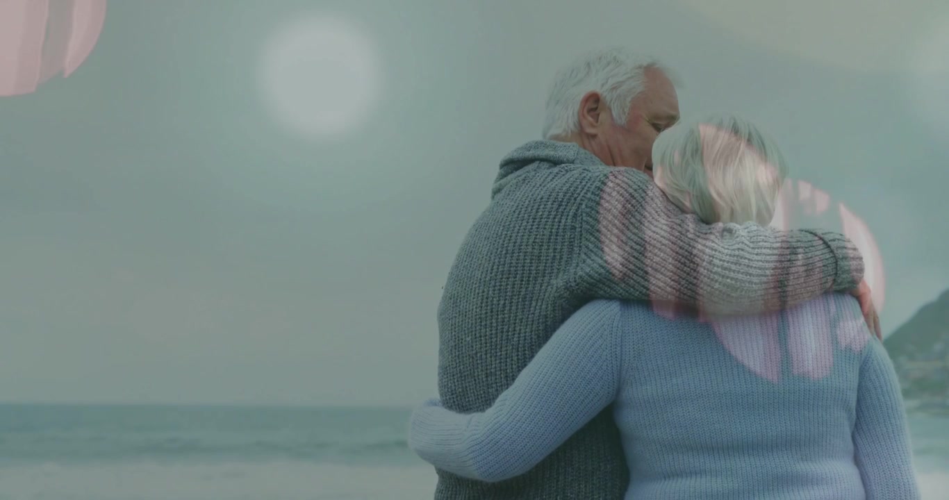 Video verticale: Anziani di fronte al mare con effetto bokeh, mentre due uomini si abbracciano e si baciano, evocando benessere.