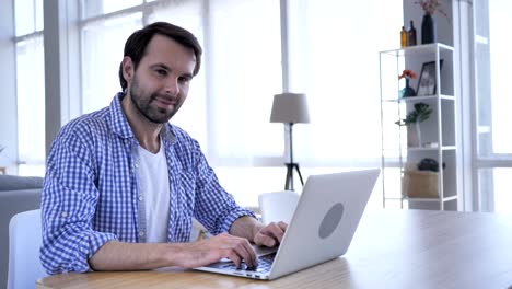 man smiling while looking at camera at work, typing on laptop ,4k , high quality