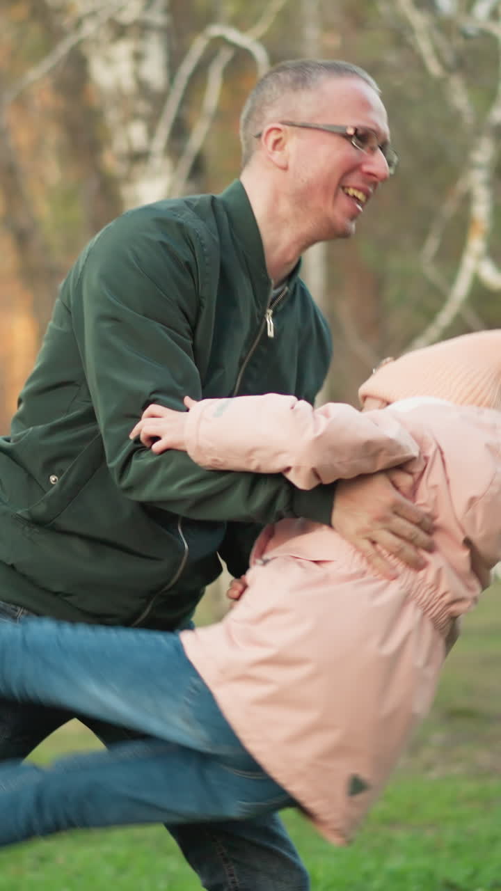un hombre con una chaqueta verde y una niña pequeña con una jaqueta rosa, ambos con vaqueros azules, están jugando alegremente juntos al aire libre en un campo de hierba verde exuberante
