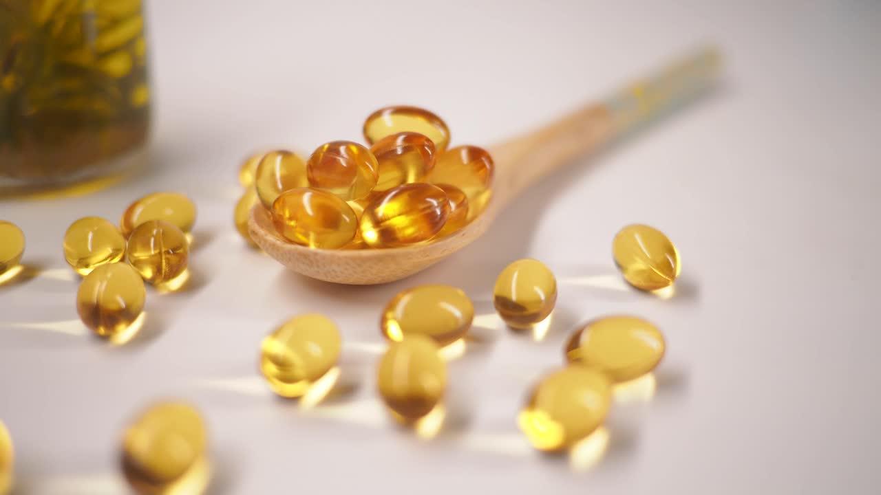 Capsule di gel gialle su un cucchiaio di legno e sparse su una superficie bianca