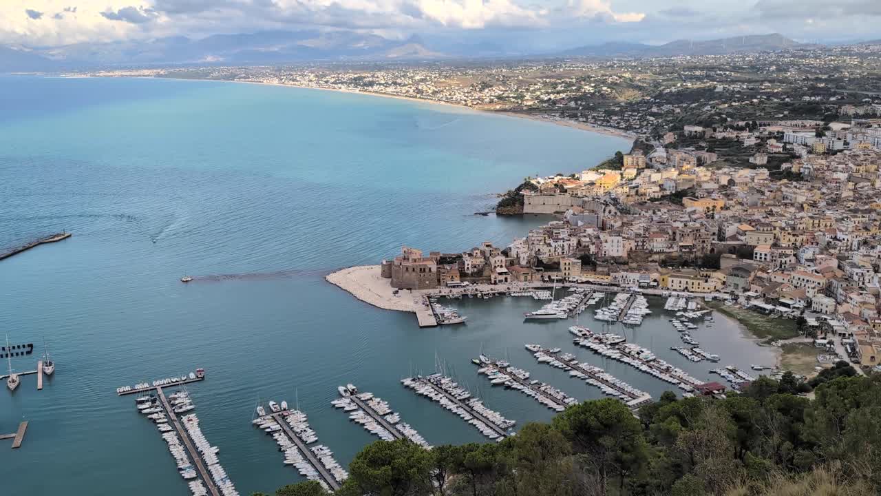 Pan-right hillside view of Castellammare del Golfo, showing the full coastline, marina, and medieval castle along the Sicilian shore. Wide, scenic daylight look over the bay and town