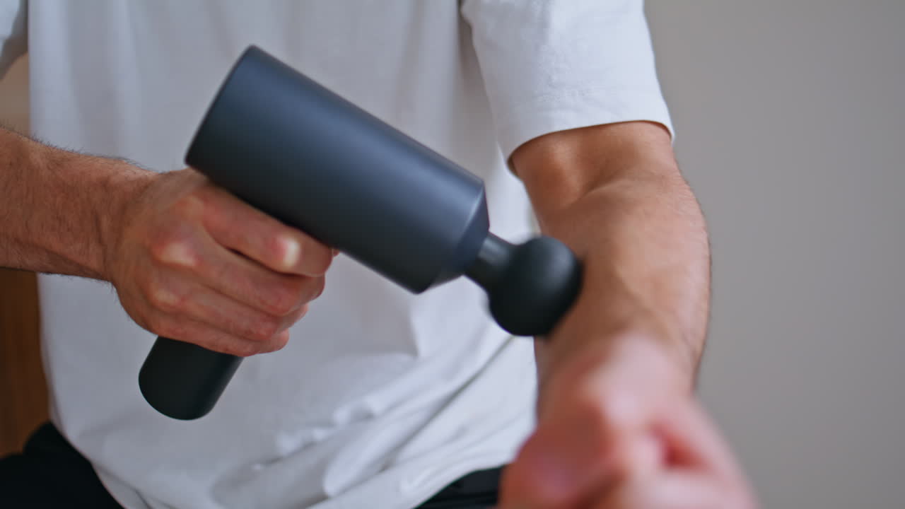 Massage gun massaging arm after sport activity in apartment closeup. Sportsman