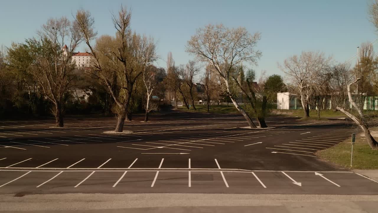Empty parking lot with trees during the COVID-19 pandemic. Aerial crane ascending shot revealing the city in the background.