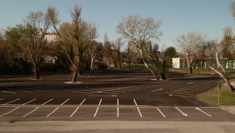 empty parking lot with trees during the covid-19 pandemic. aerial crane ascending shot revealing the city in the background.