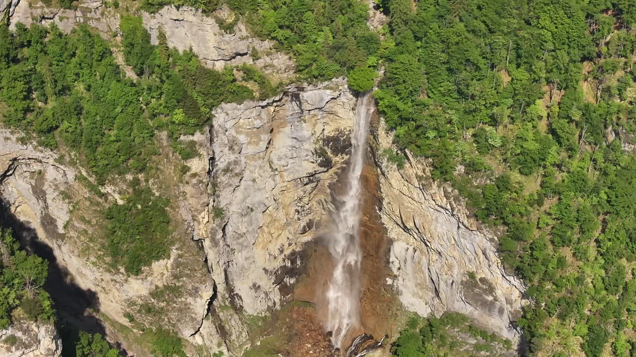 Top-down aerial view of Seerenbachfälle waterfall, cutting through rugged cliffs and green forest in Switzerland. A striking display of vertical flow and wild alpine terrain