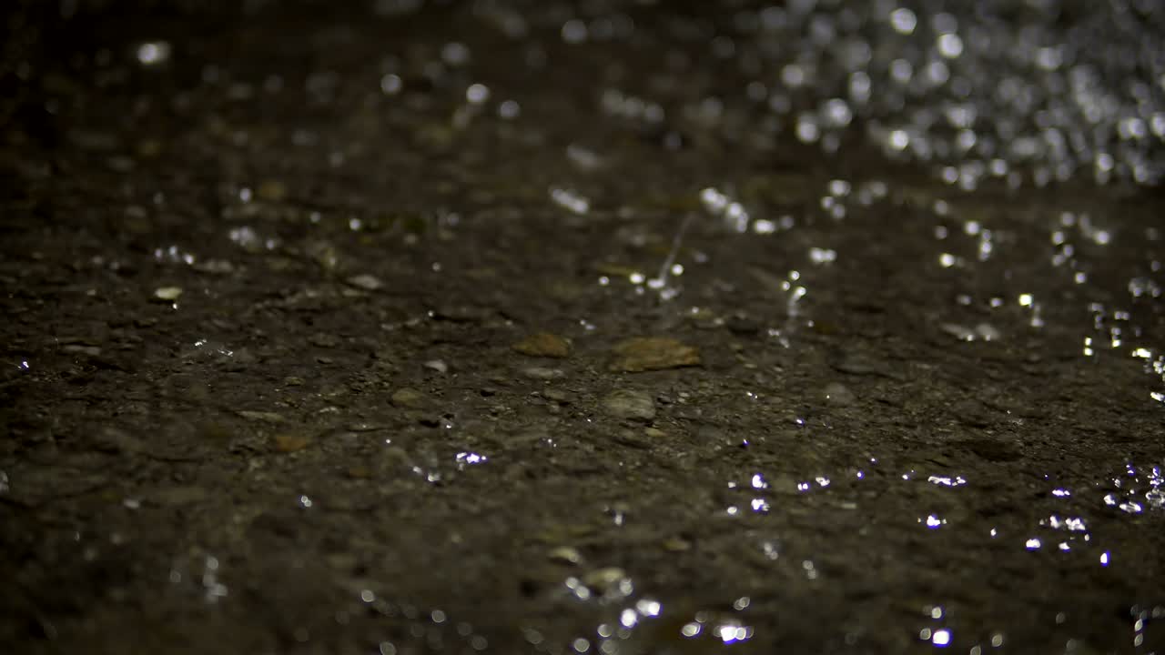 Rain on asphalt road at night, closeup background loop