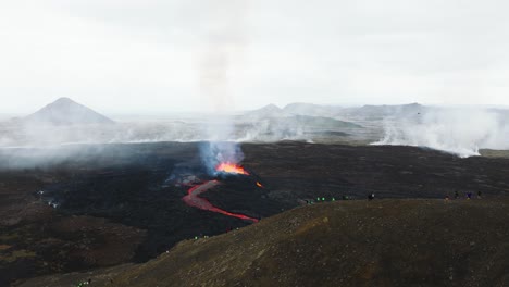 Aerial-landscape-view-of-many-people-looking-at-the-volcanic-eruption-at-Litli-Hrutur,-Iceland,-with-fresh-lava-and-smoke-coming-out