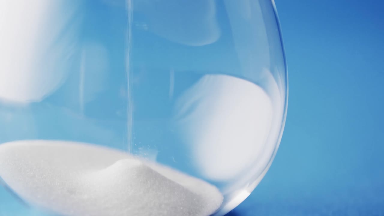 video de primer plano de un reloj de arena con arena blanca vertiendo con espacio de copia sobre fondo azul