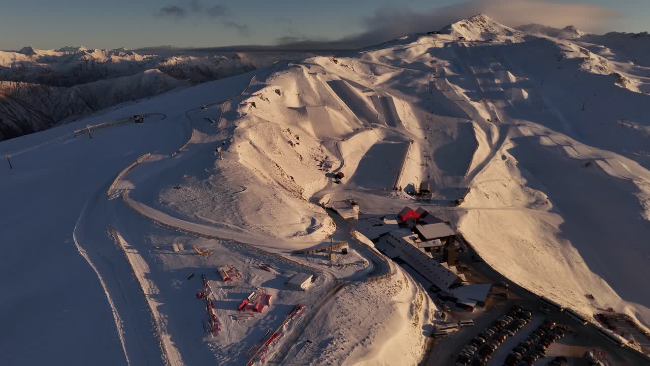Cardrona ski resort at sunrise, chairlifts, and majestic snow-covered mountains in background. New Zealand. Aerial drone