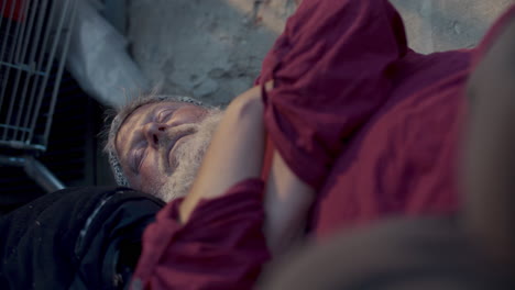 elderly homeless man sleeping on street near weathered wall