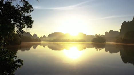 Drohne-Fliegt-Aus-Dem-Wald-Durch-Den-Nong-Thale-See-Mit-Kalksteinbergen-Bei-Sonnenaufgang-Mit-Bewegungsnebel,-Krabi,-Thailand