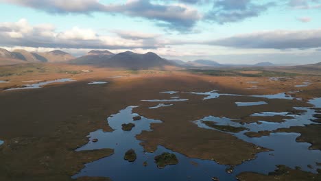 wide aerial shot of connemara lakes with calm lakes in the foreground and beanna beola mountain range in the distance, slowly panning drone shot