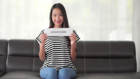 asian woman wearing casual clothes shows the written on paper message with the hashtag stay home