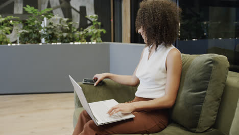 Happy-biracial-businesswoman-using-laptop-and-smartphone-in-office-lounge,-in-slow-motion