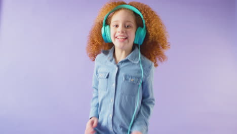 studio shot of girl wearing headphones and dancing against purple background