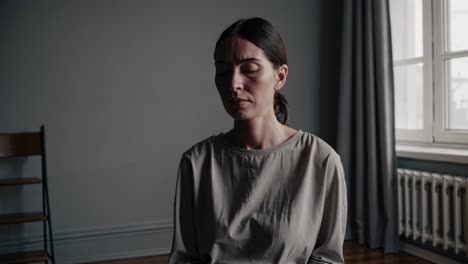 Moody video scene with a woman sitting in a dimly lit room. Shot from a straight-on angle