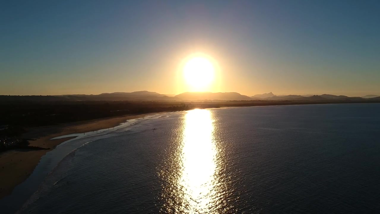 Aerial reflection of beautiful sunset behind the mountains with waves over the beach. Byron Bay, New South Wales, Australia.