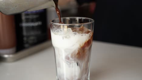 Barista-stainless-pitcher-pours-espresso-and-mocha-sauce-into-glass-of-ice-and-milk,-slow-motion-4K