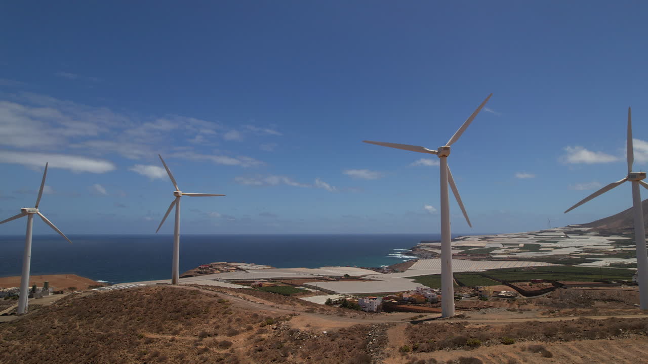 Aerial pull back from alternate energy wind farm turbines rotating alongside coastal seascape