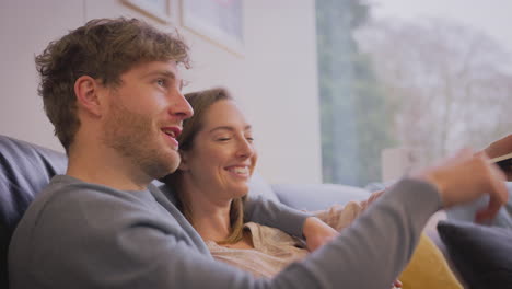 Amorosa-Pareja-Embarazada-Sentada-En-Un-Sofá-En-Casa-Juntos-Viendo-Televisión-En-Casa