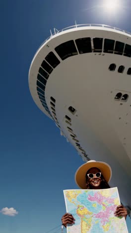 Low-angle shot of a woman holding a map under a cruise ship&#039;s bow, capturing a travel adventure