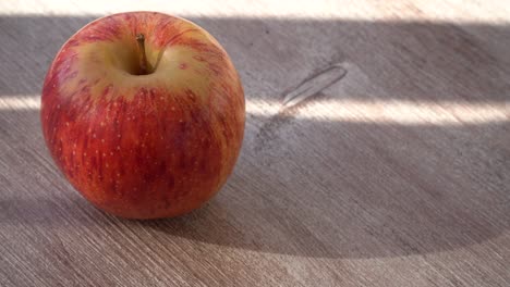 ripe apple on a wooden background. sun shadow falls on the fruit