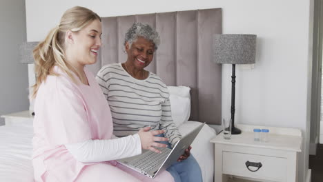 caucasian female nurse and senior african american woman using laptop, copy space, slow motion