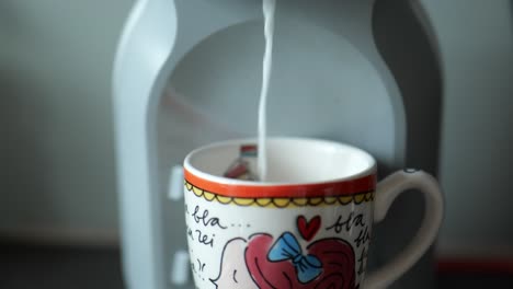 milk being dispensed into colourful mug from coffee machine indoors