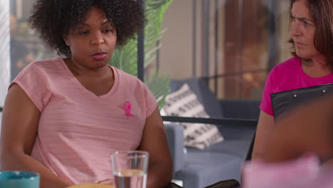 group of women wearing pink breast cancer awareness ribbons meeting and talking at therapy support group for cancer treatment patients 8